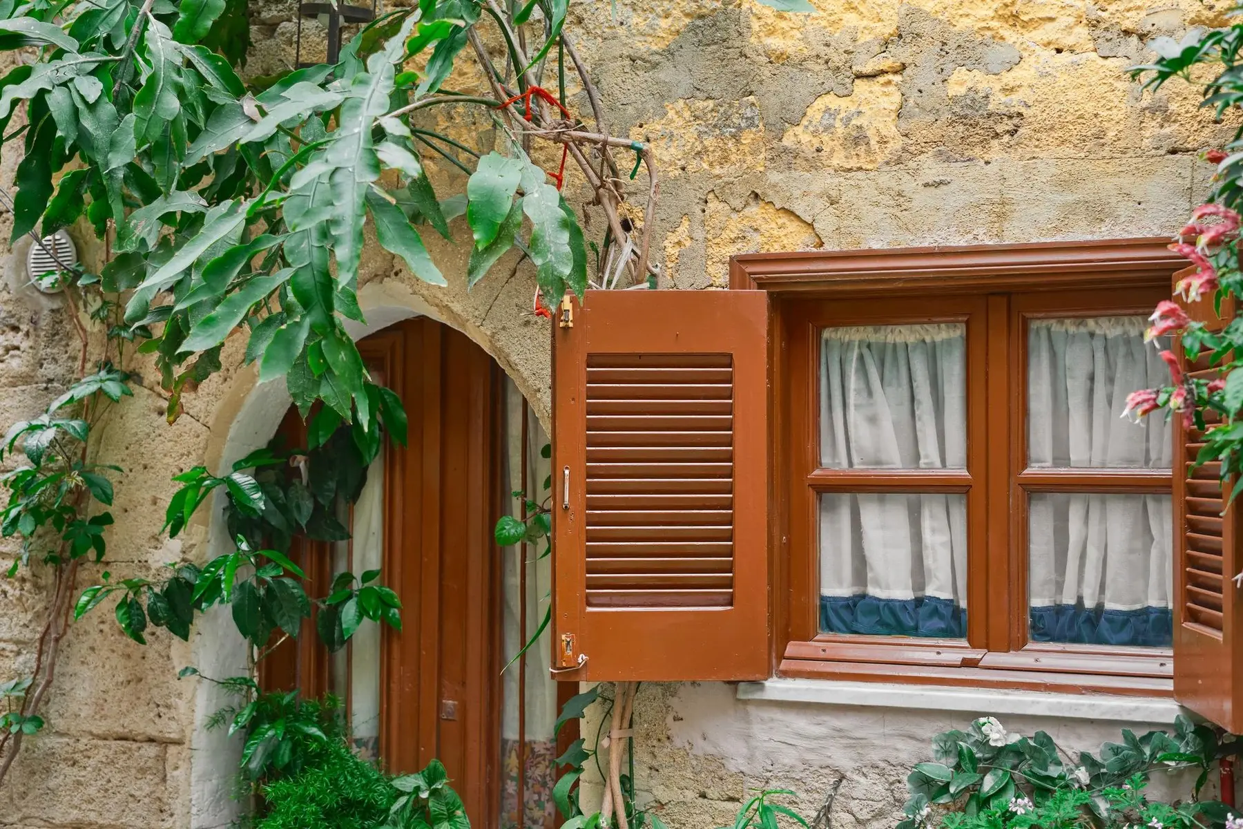 Façade en pierre ocre avec un volet bois repeint et une fenêtre à petits bois