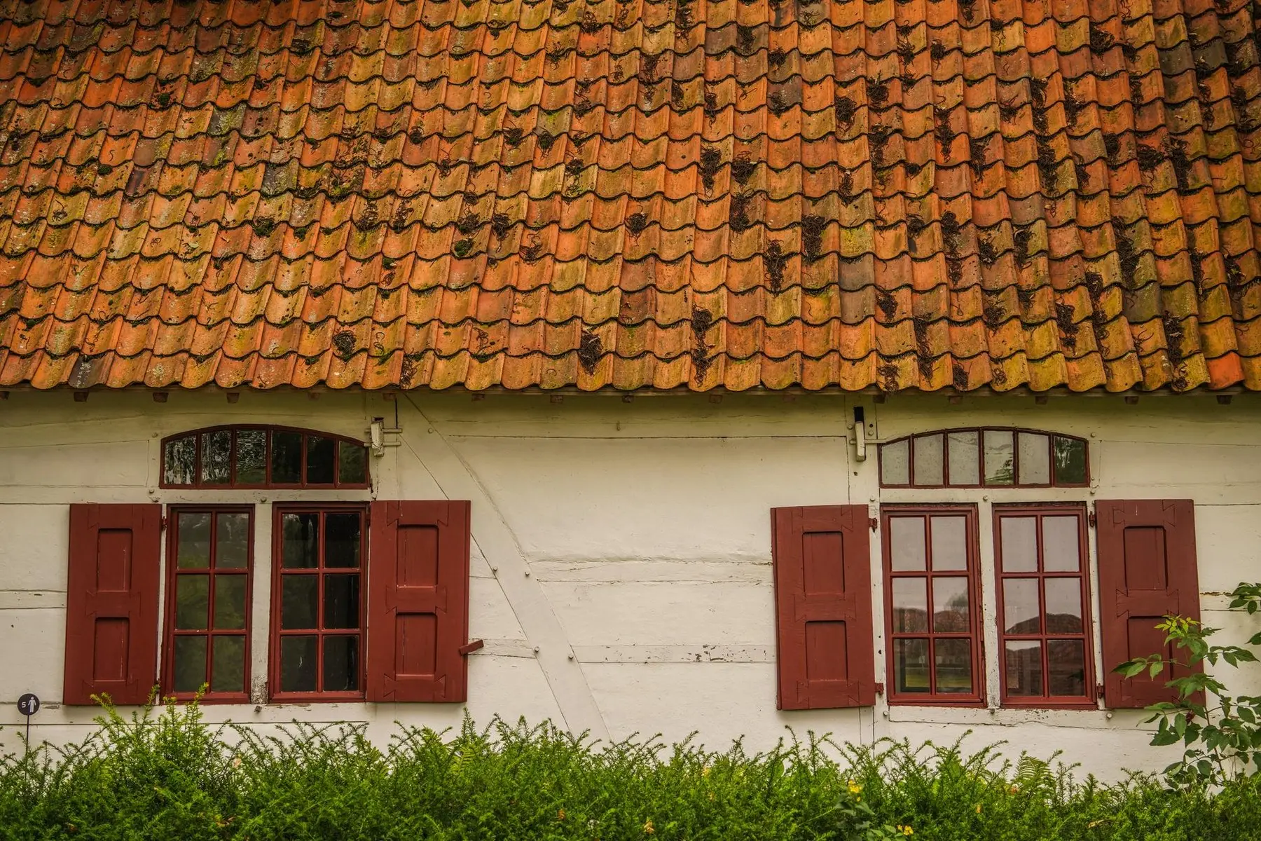 Toiture en tuile plate au-dessus d’une façade enduite à volets bois